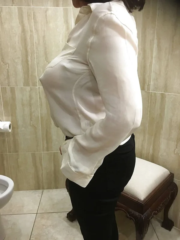 Femme de profil en chemise blanche et pantalon noir dans une salle de bain avec carreaux de marbre.