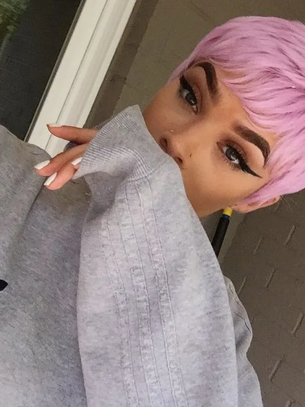 Portrait de profil d'une personne aux cheveux roses courts, portant un sweat-shirt gris Adidas, regardant vers l'objectif.