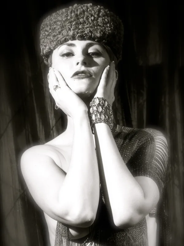 Portrait en noir et blanc, chapeau à poils, mains sur le visage, bijoux, robe texturée, éclairage dramatique